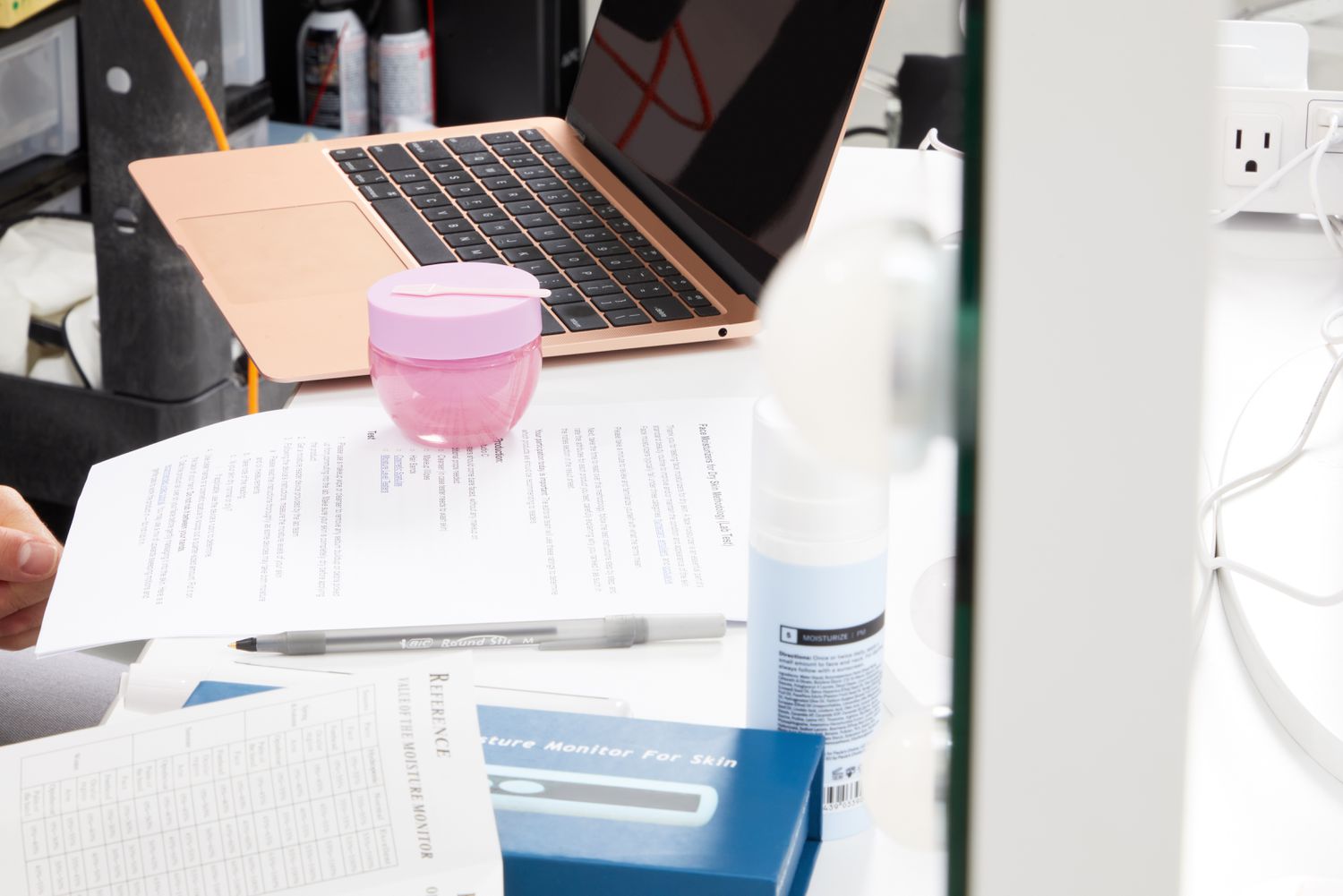 A jar of Glow Recipe Plum Plump Refillable Hyaluronic Acid Moisturizer on counter on top of documents next to a laptop