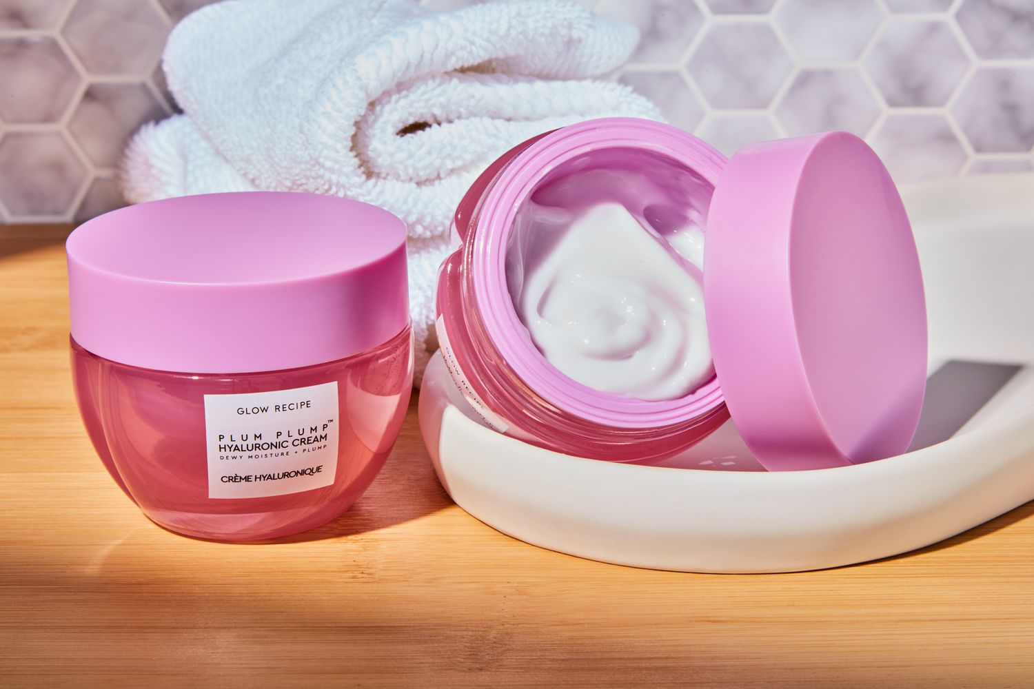 Jars of Glow Recipe Plum Plump Hyaluronic Cream displayed on a wooden surface next to a towel